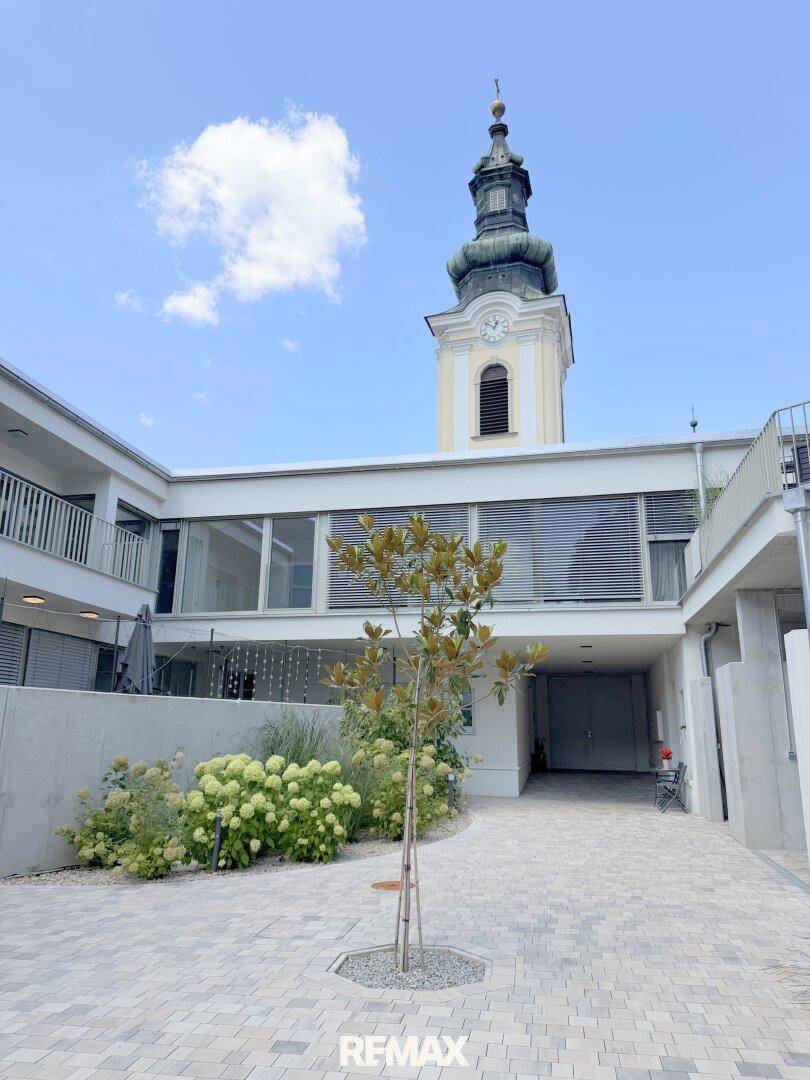 Gepflasterter Innenhof mit jungem Baum und Blick auf den historischen Kirchturm.