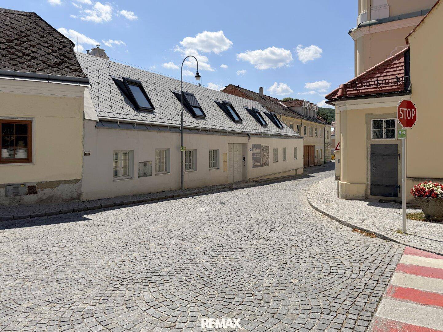 Historische Kopfsteinpflasterstraße mit alten Gebäuden und einem Kirchturm im Hintergrund.