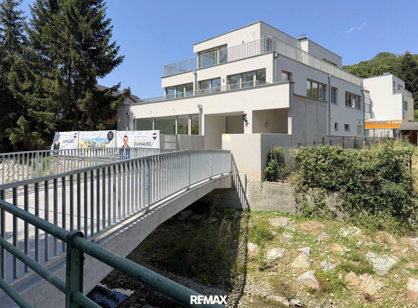 Modernes Mehrfamilienhaus mit weißer Fassade, großen Fenstern und Balkonen, umgeben von viel Grün.