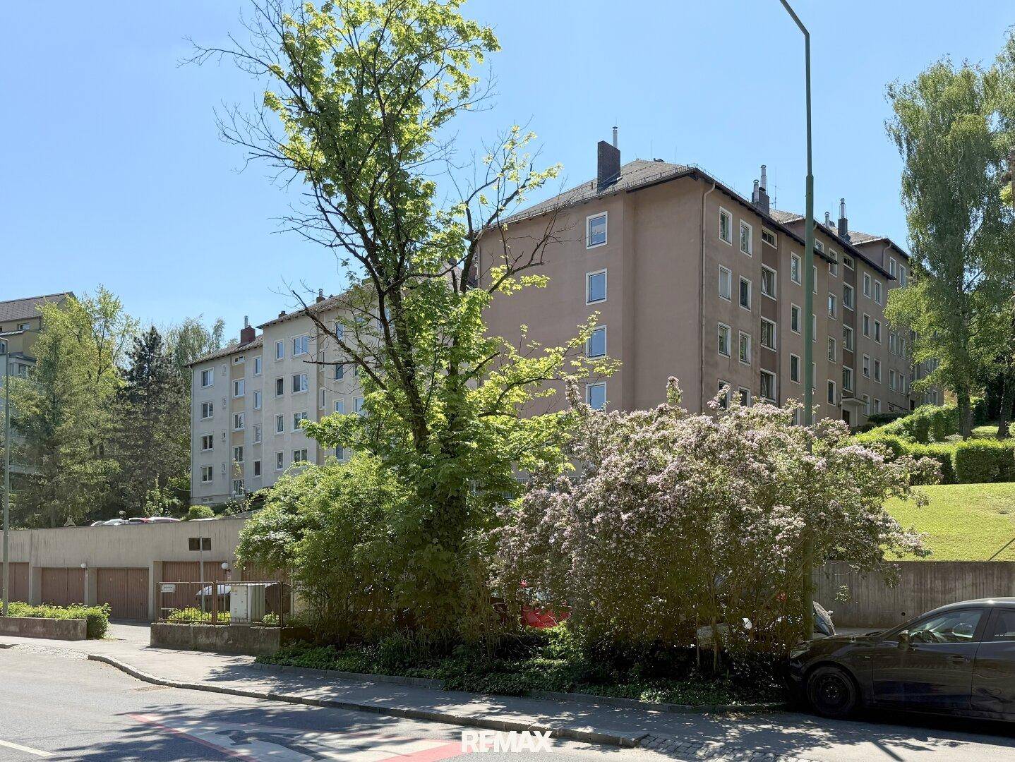 Mehrfamilienhaus mit mehreren Etagen, umgeben von Bäumen und Grünflächen in einer ruhigen Gegend.