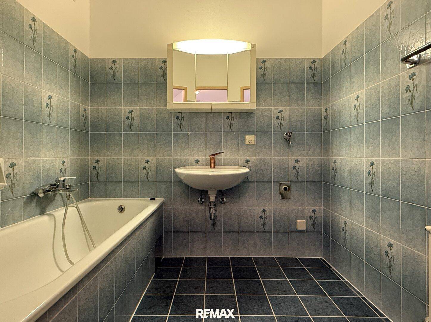 Badezimmer mit blauen Blumenfliesen, Badewanne und Waschbecken mit Spiegelschrank im Retro-Stil.
