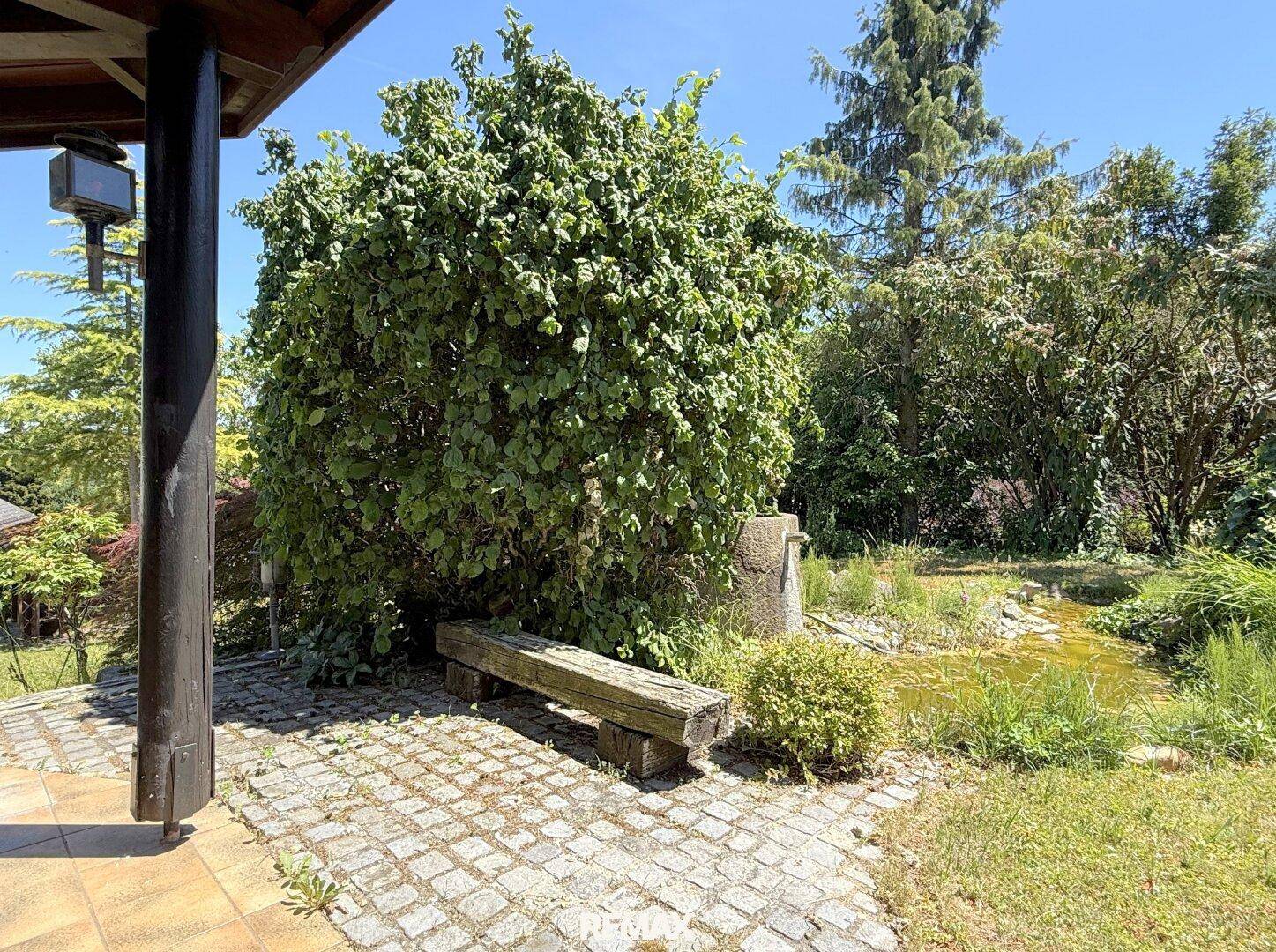 Idyllischer Gartenbereich mit kleinem Teich, Steinweg und rustikaler Holzbank.