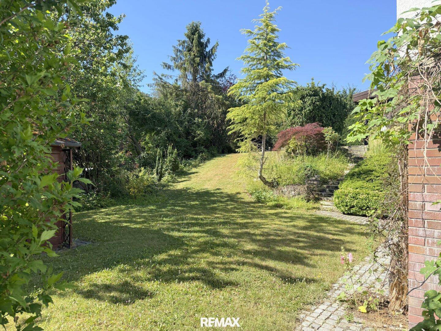 Gepflegter Garten mit Rasenfläche, Bäumen und Treppen.