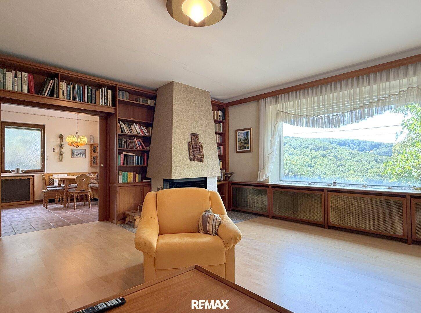 Gemütliches Wohnzimmer mit Kamin, Holzbücherregalen und Blick ins Grüne.