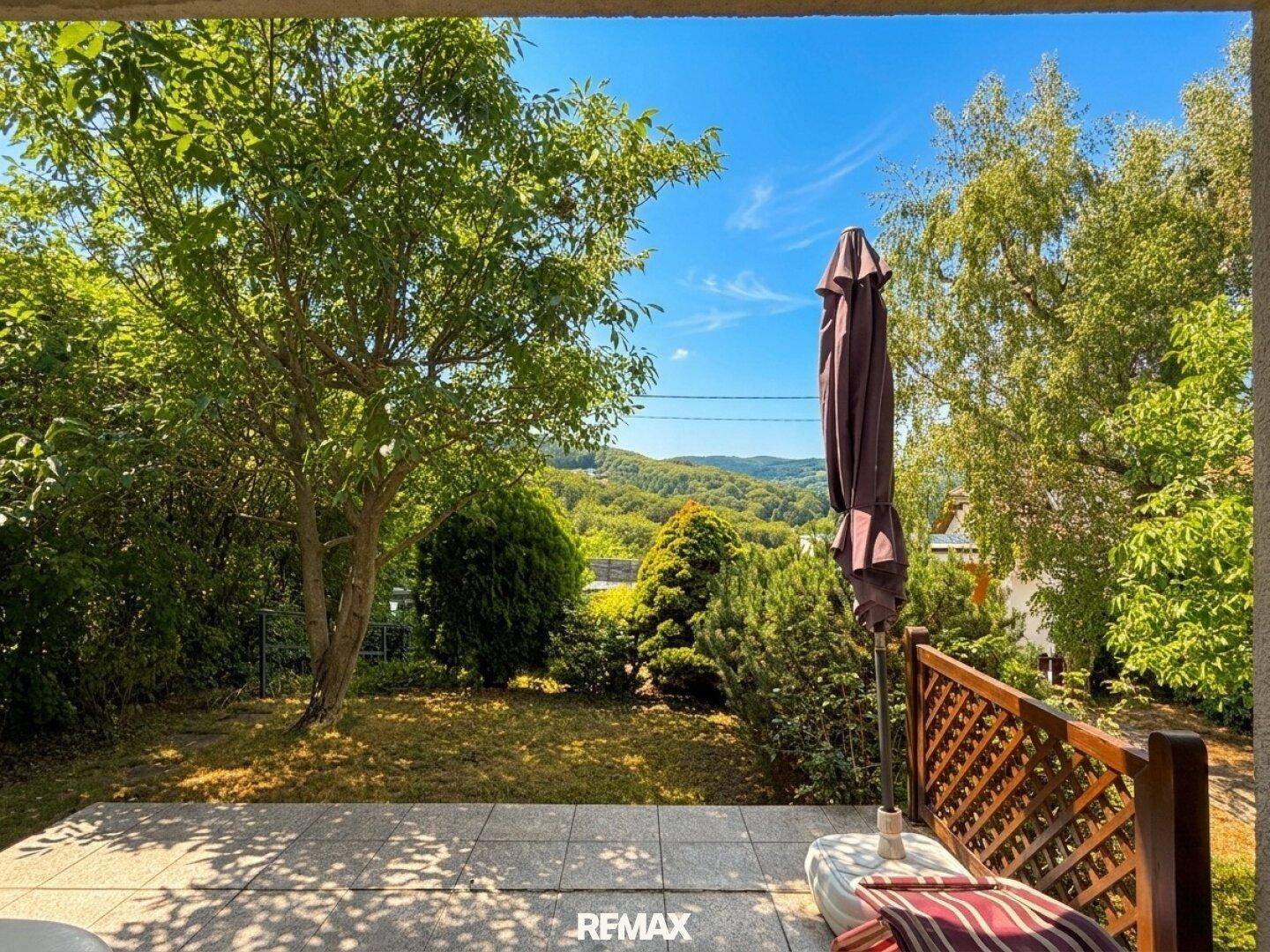 Sonniger Terrassenbereich mit Schirm und Blick auf die grüne Hügellandschaft.