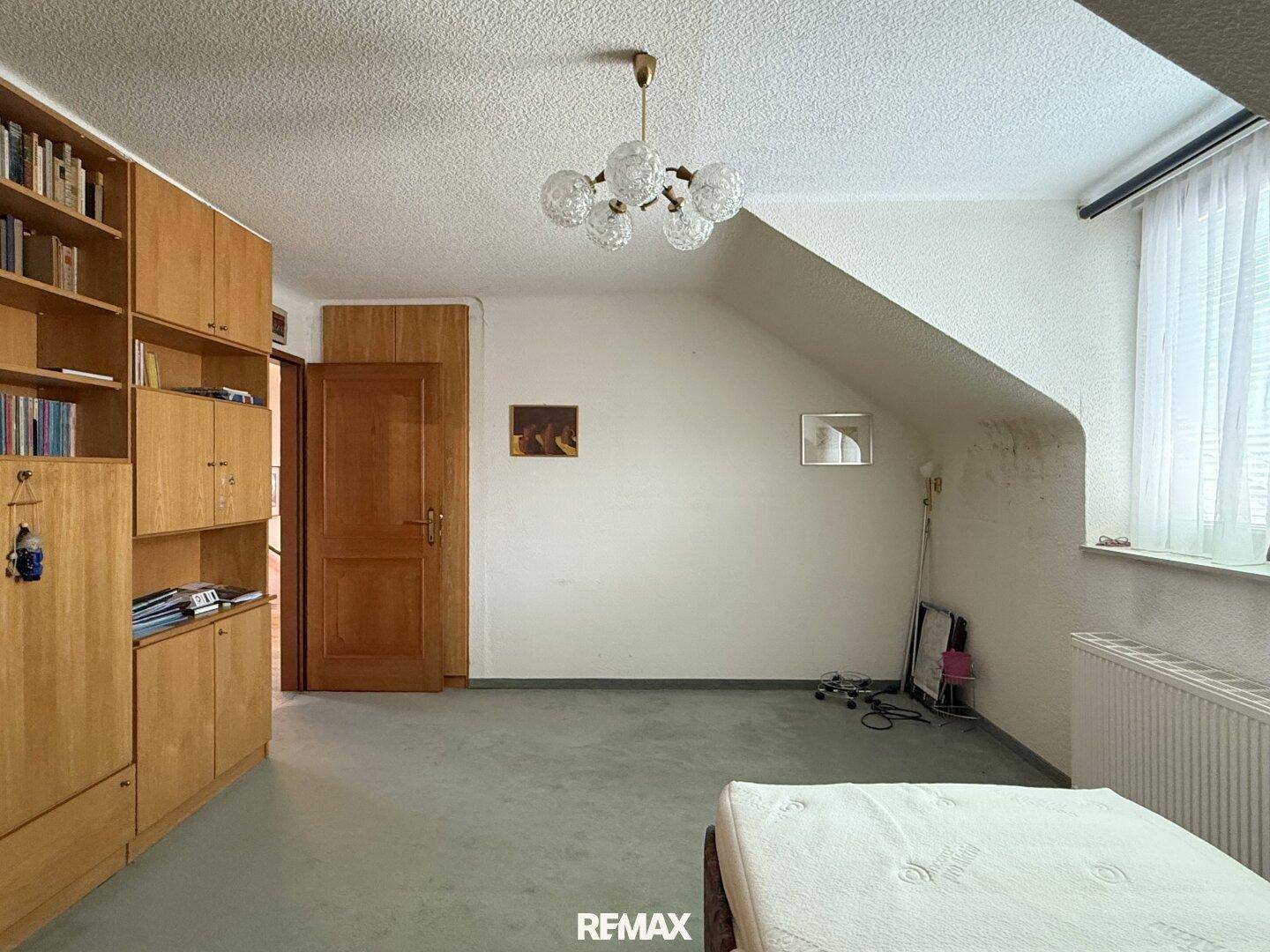 Dachgeschosszimmer mit Schräge, Einbauschränken und einfacher Einrichtung.