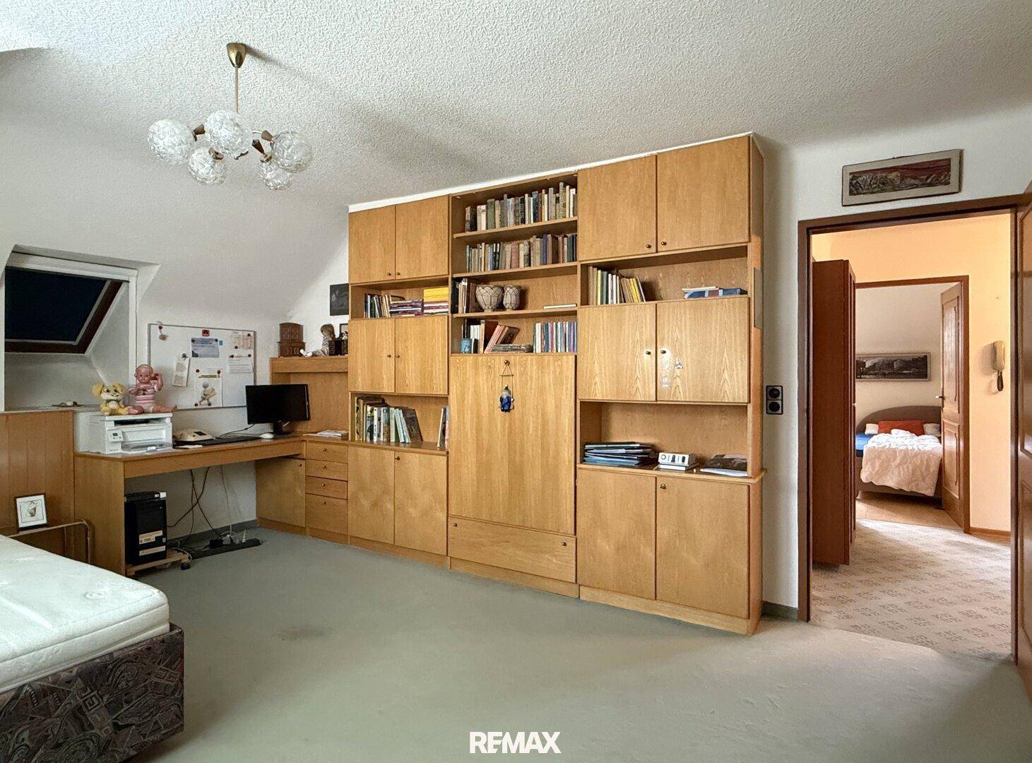 Geräumiges Dachgeschosszimmer mit Schräge, Einbauschränken und Schreibtischbereich.