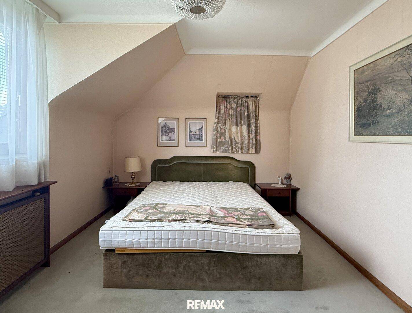 Schlafzimmer im Dachgeschoss mit Schräge, Doppelbett und traditioneller Tapete.