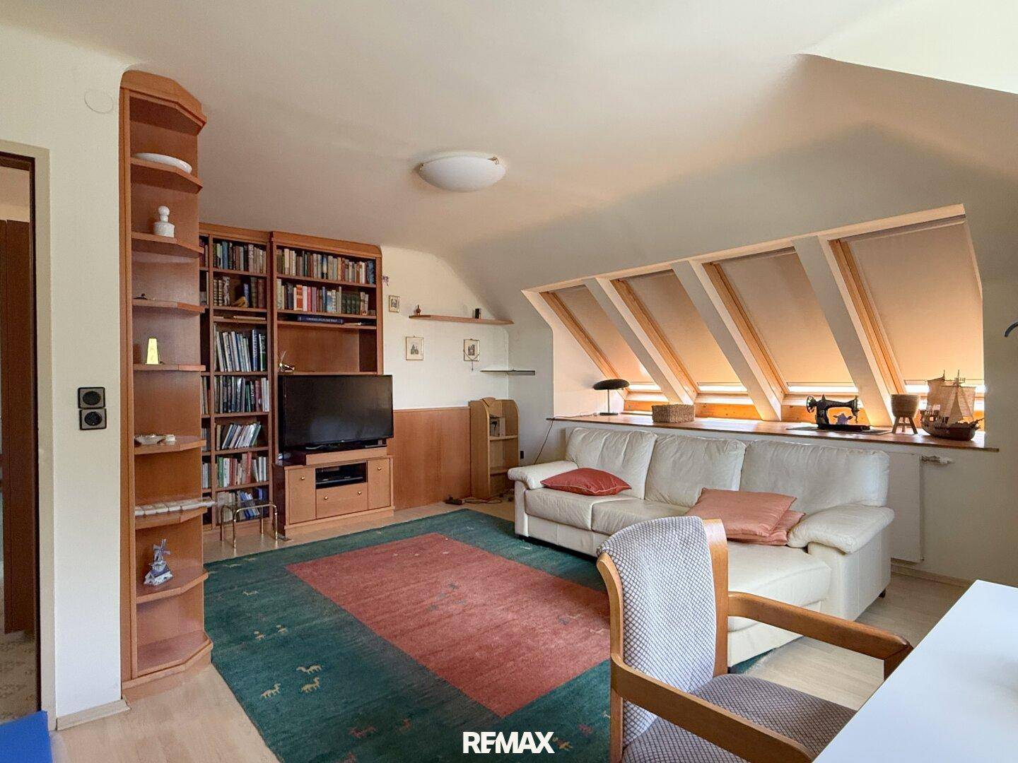 Gemütliches Dachgeschoss-Wohnzimmer mit Schrägen, Sofa und Bücherregal.