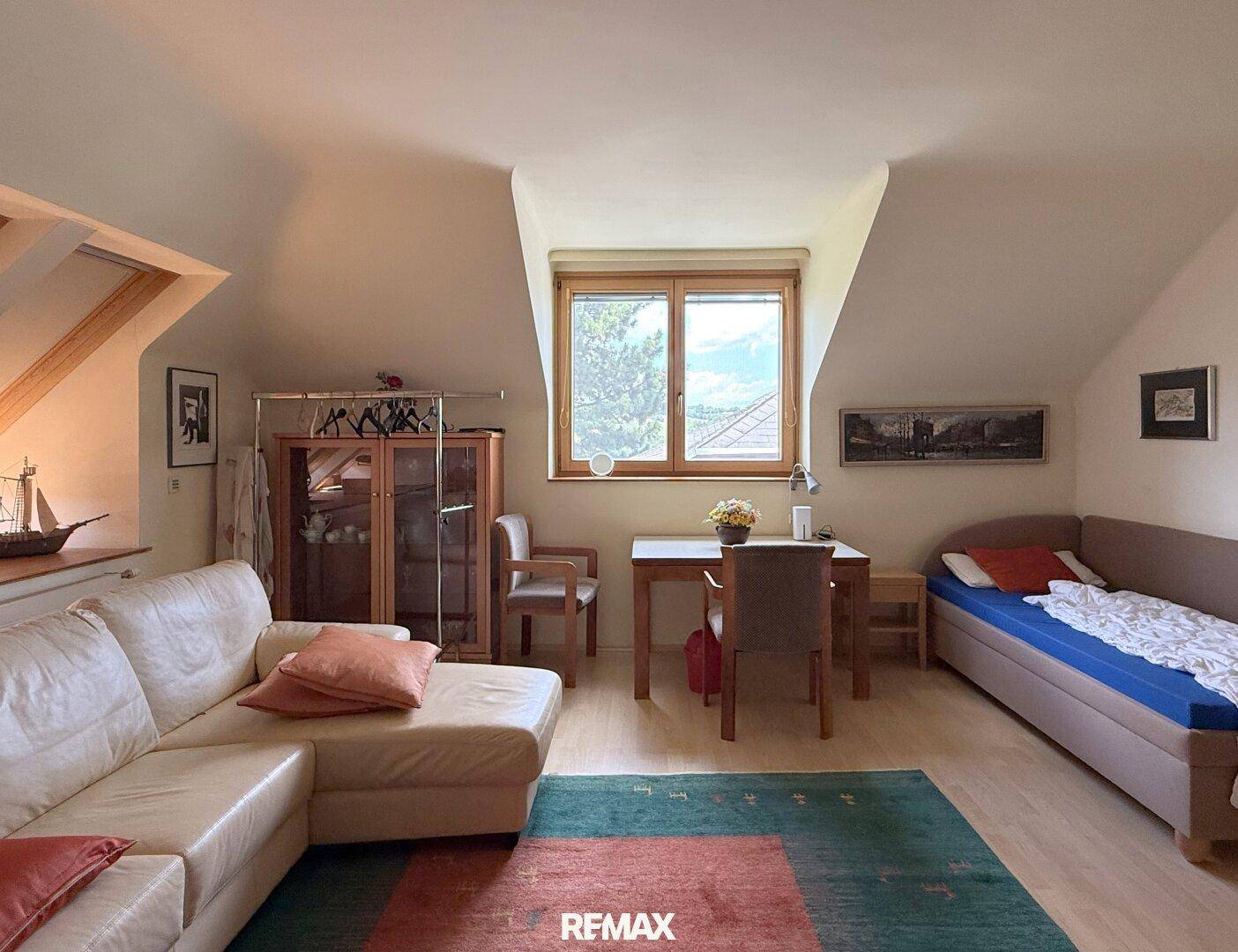 Helles Dachgeschoss-Wohnzimmer mit Schrägen, Sofa und Blick ins Grüne.