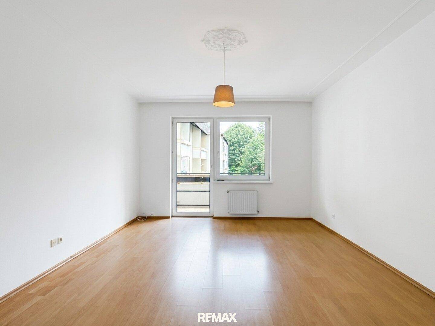 Helles Wohnzimmer mit Parkettboden, weiß gestrichenen Wänden und direktem Balkonzugang.