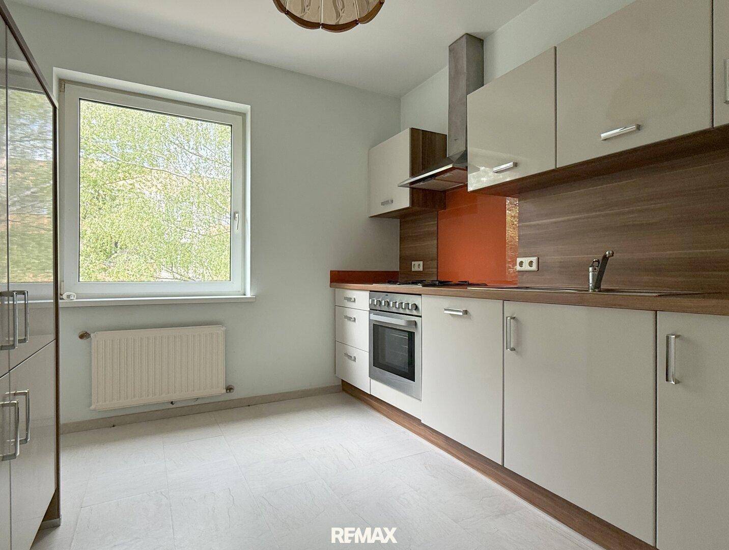 Moderne Küche mit hellgrauen Schränken, Holzarbeitsplatte und orangefarbener Rückwand, inklusive Fenster.