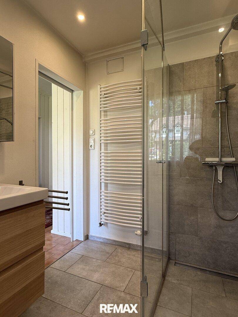 Helles Badezimmer mit großer Duschkabine, Handtuchheizkörper und modernen Fliesen.