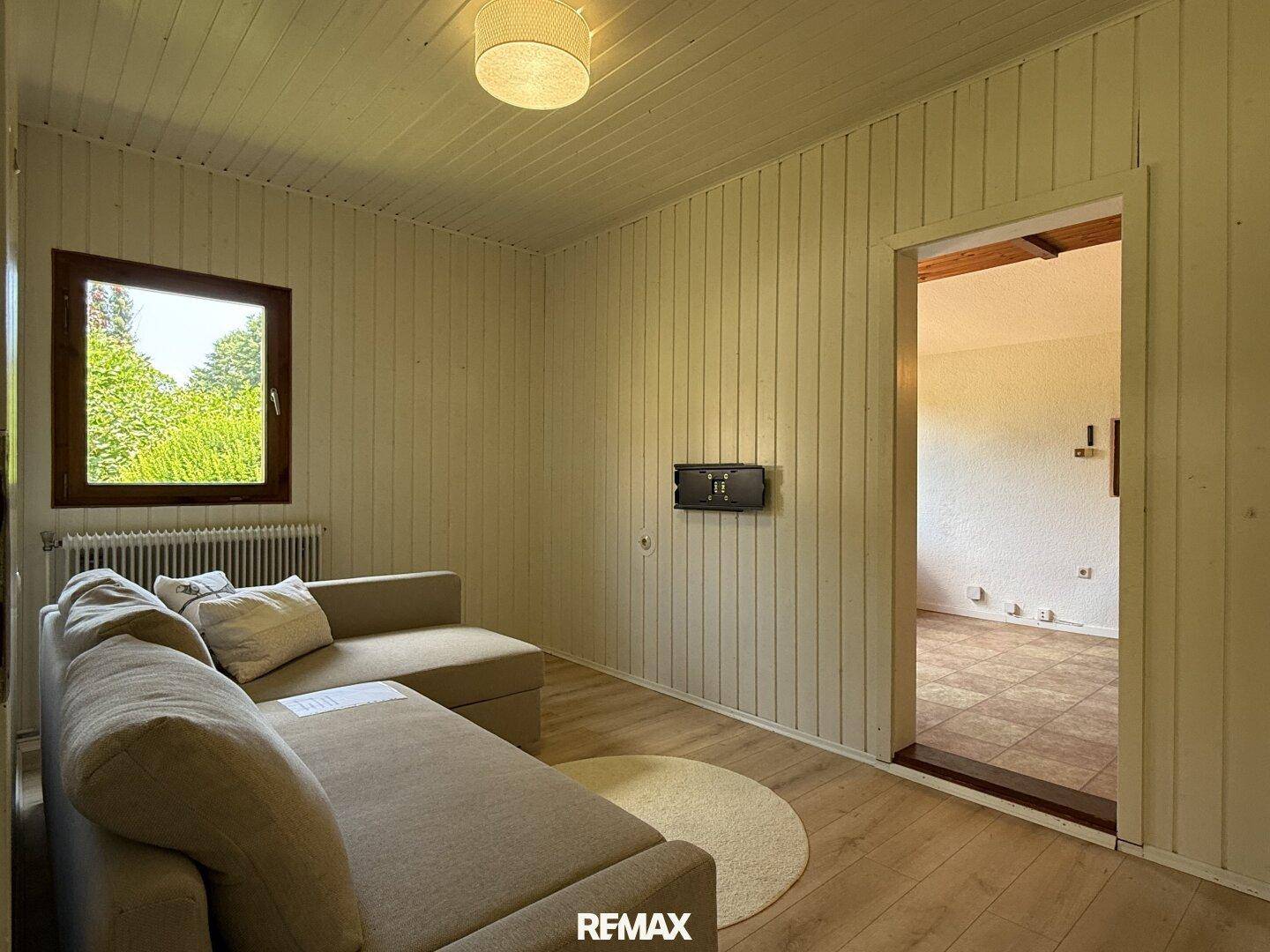 Gemütliches Wohnzimmer mit holzvertäfelten Wänden und hellem Laminatboden.
