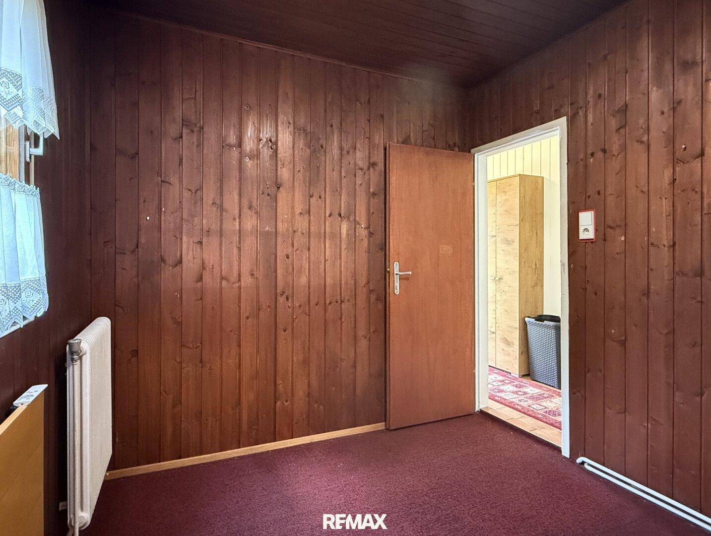 Einfaches Zimmer mit Holzwänden und Teppichboden, ideal als Schlaf- oder Gästezimmer.