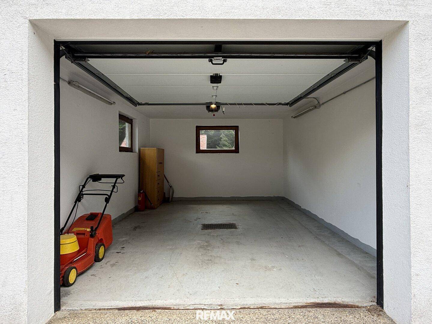 Geräumige Garage mit Betonboden, Fenster und Platz für Fahrzeuge und Gartengeräte.