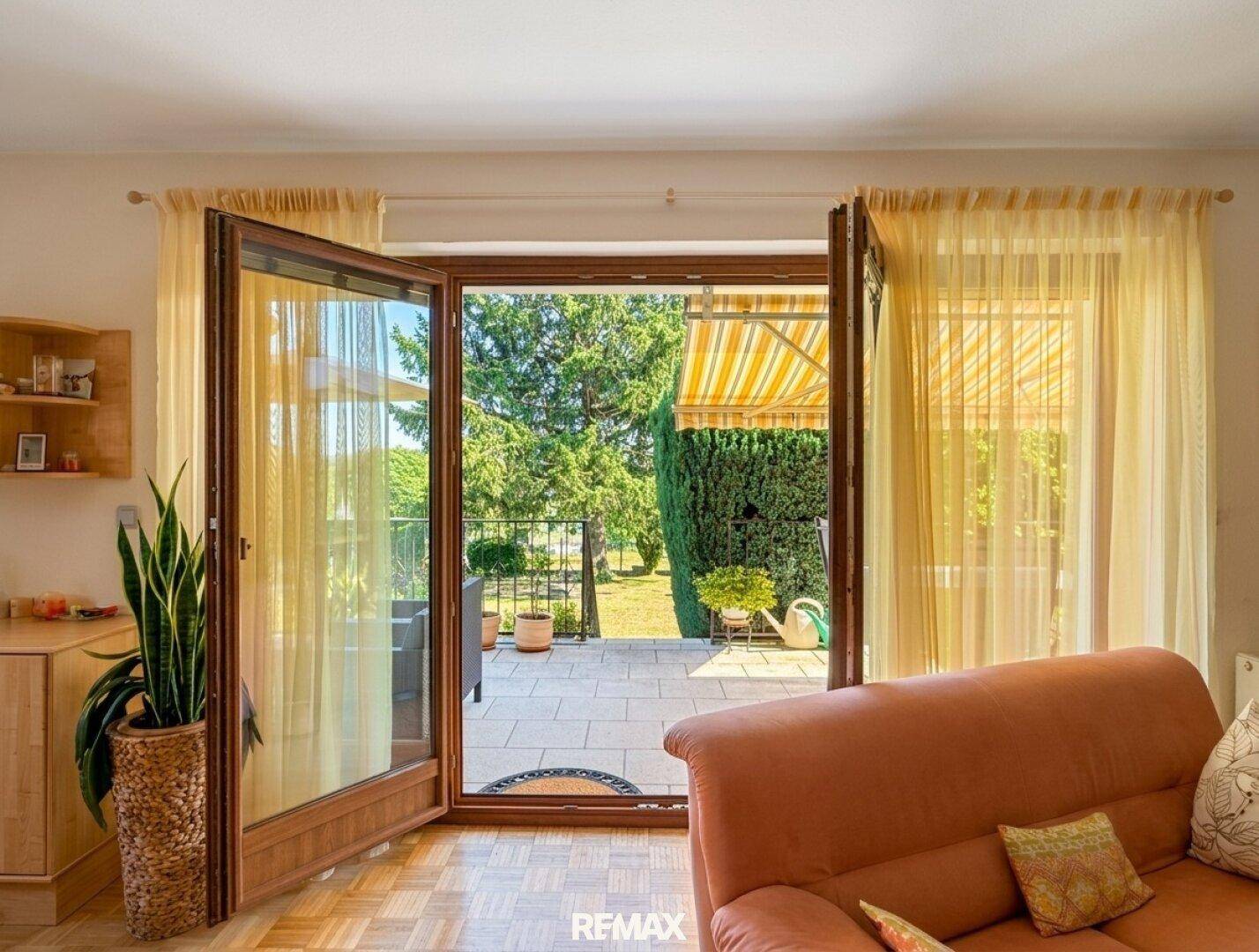 Wohnzimmer mit großen Fenstern und direktem Zugang zur sonnigen Terrasse.