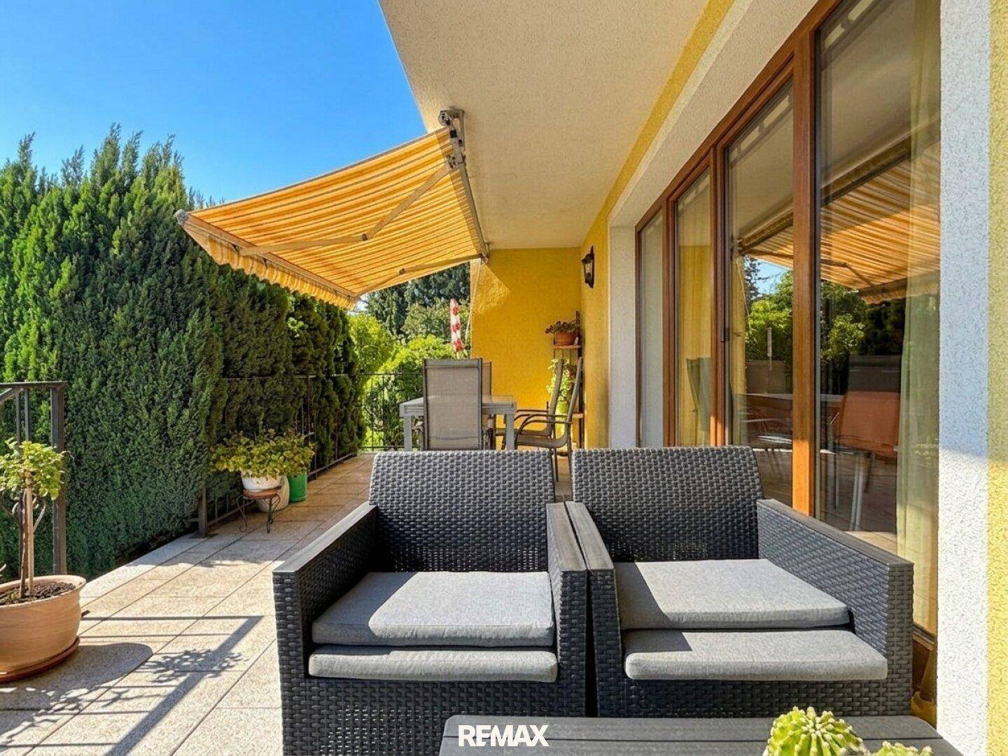 Sonnige Terrasse mit Markise, Gartenmöbeln und Blick ins Grüne.