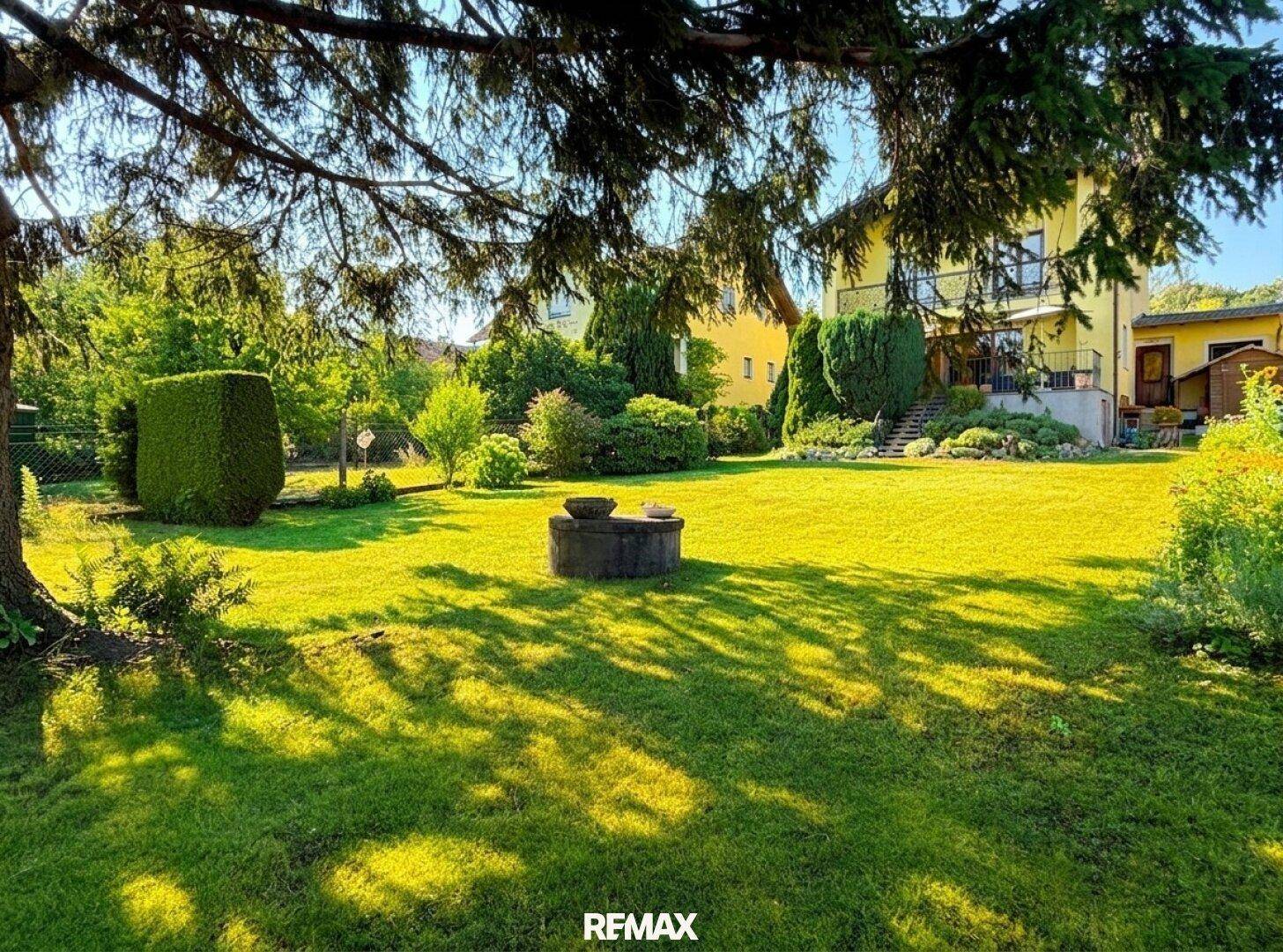 Großer, sonniger Garten mit altem Baumbestand und einem Brunnen.