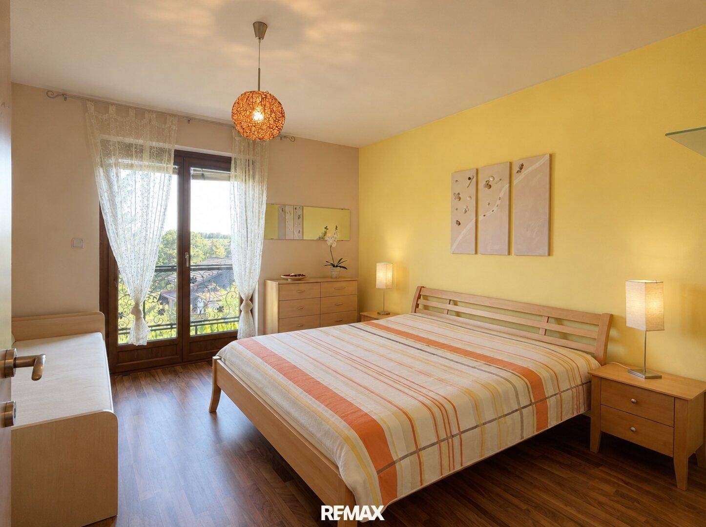 Helles Schlafzimmer mit Holzbett, Laminatboden und Balkonzugang.