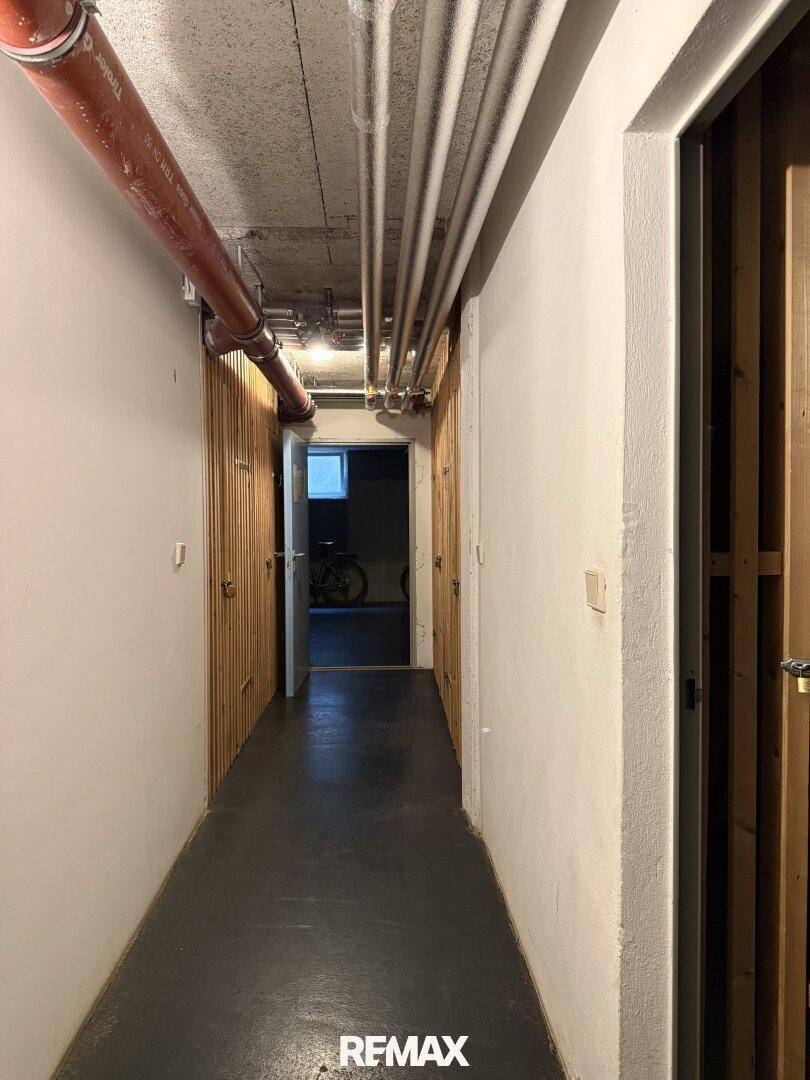 Kellerflur mit sichtbaren Rohren an der Decke und Türen zu den Abstellräumen.