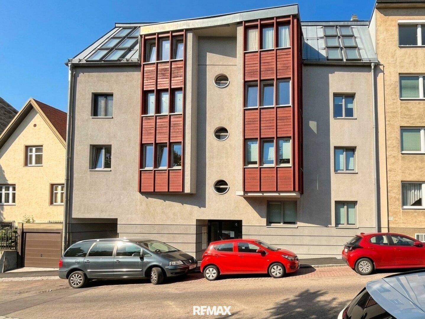 Moderne Gebäudefassade mit roten Holzelementen, großen Fenstern und Mansarddach.