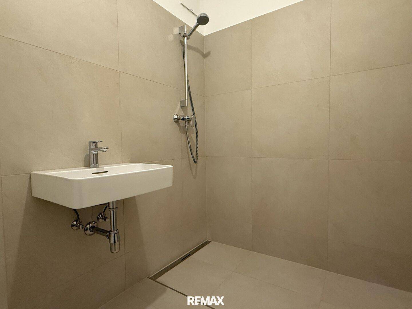 Modernes Badezimmer mit beigefarbenen Fliesen, ebenerdiger Dusche und einem einzelnen Waschbecken.