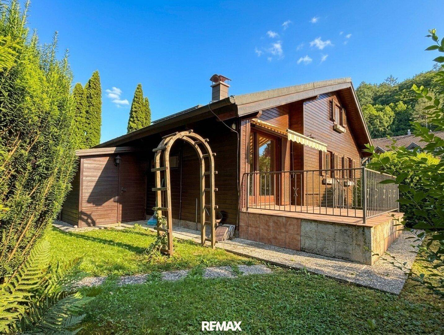 Seitlicher Blick auf das Holzhaus mit kleiner Terrasse und üppigem Grün im Garten.