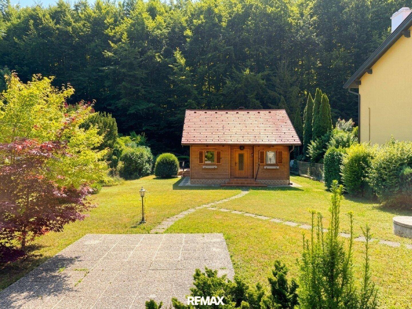 Großer Garten mit Rasenfläche und Terrasse, umgeben von Bäumen und Sträuchern.