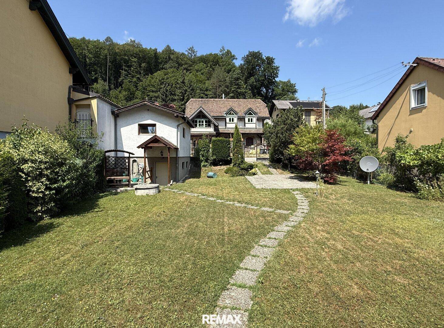 Großer, gepflegter Garten mit Rasenfläche und Steinweg, umgeben von weiteren Häusern.
