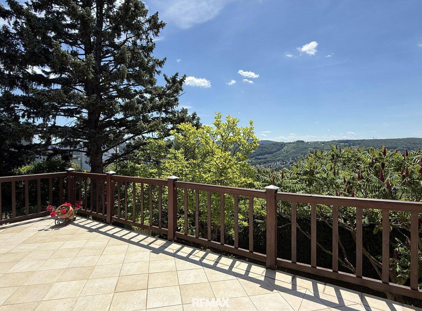 Geflieste Terrasse mit Holzgeländer und weitem Blick über die grüne Landschaft.