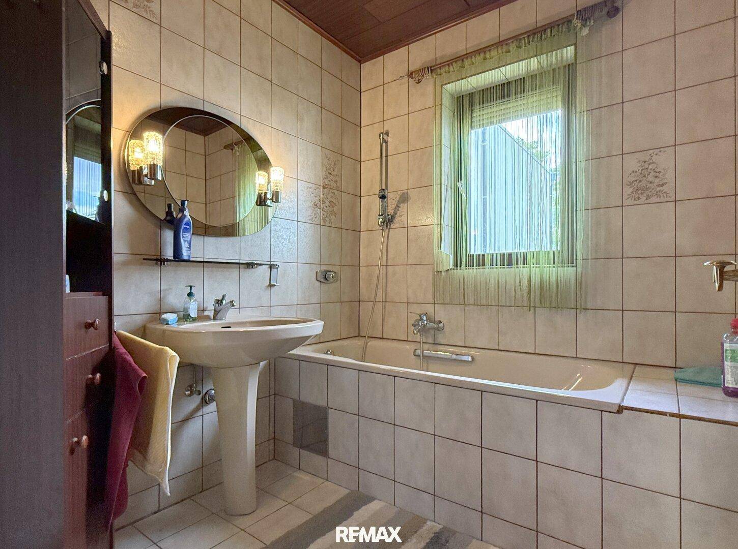 Badezimmer mit Badewanne, Waschbecken und Fliesen im 80er-Jahre-Stil.