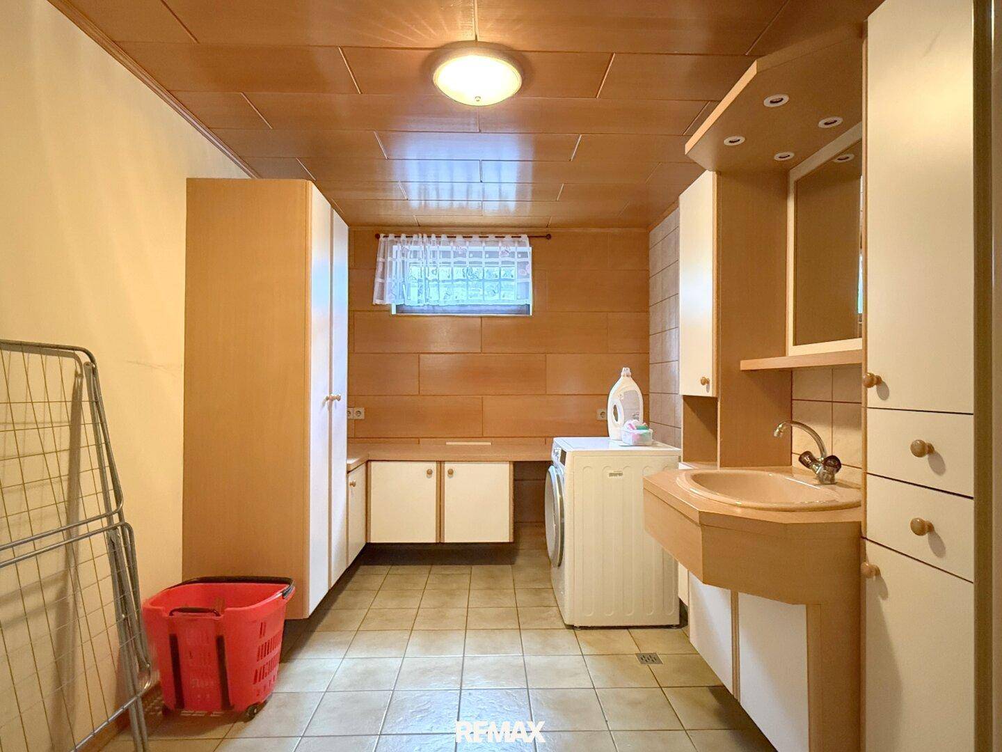 Waschküche im Keller mit Waschmaschine, Waschbecken und praktischen Schränken.