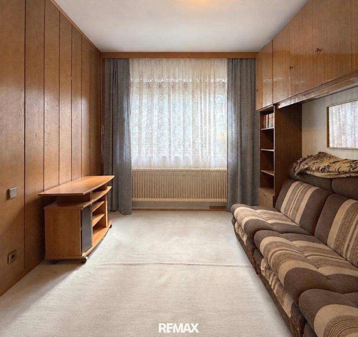 Schlafzimmer oder Gästezimmer mit Holzvertäfelung, Teppichboden und einem Sofa.