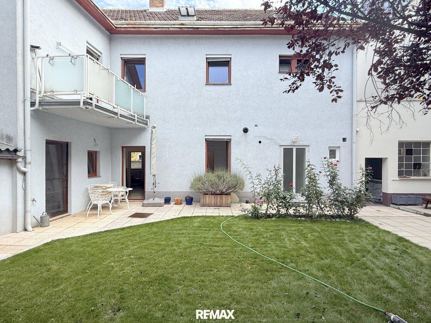 Gepflegter Gartenbereich mit Rasenfläche, gepflasterter Terrasse und Zugang zum Haus.