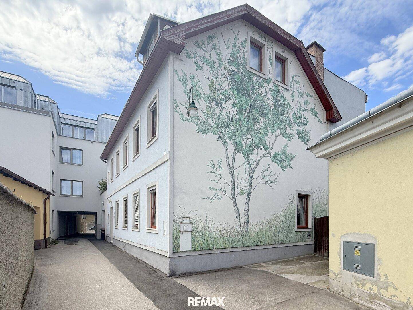 Historische Fassade eines Gebäudes mit künstlerischer Baumbemalung und Mansarddach.