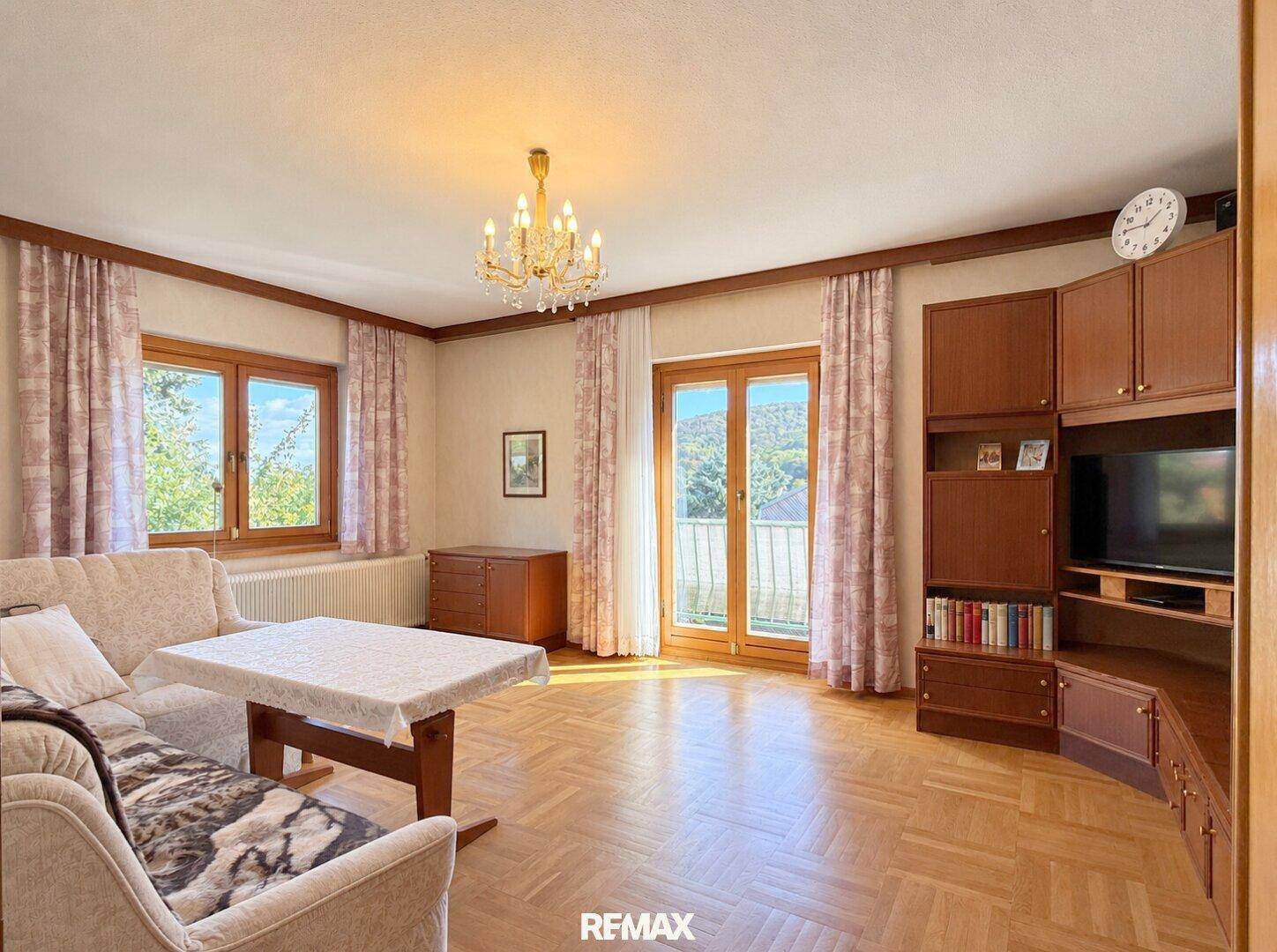 Helles Wohnzimmer mit Parkettboden, traditionellen Möbeln und Zugang zu einem Balkon.