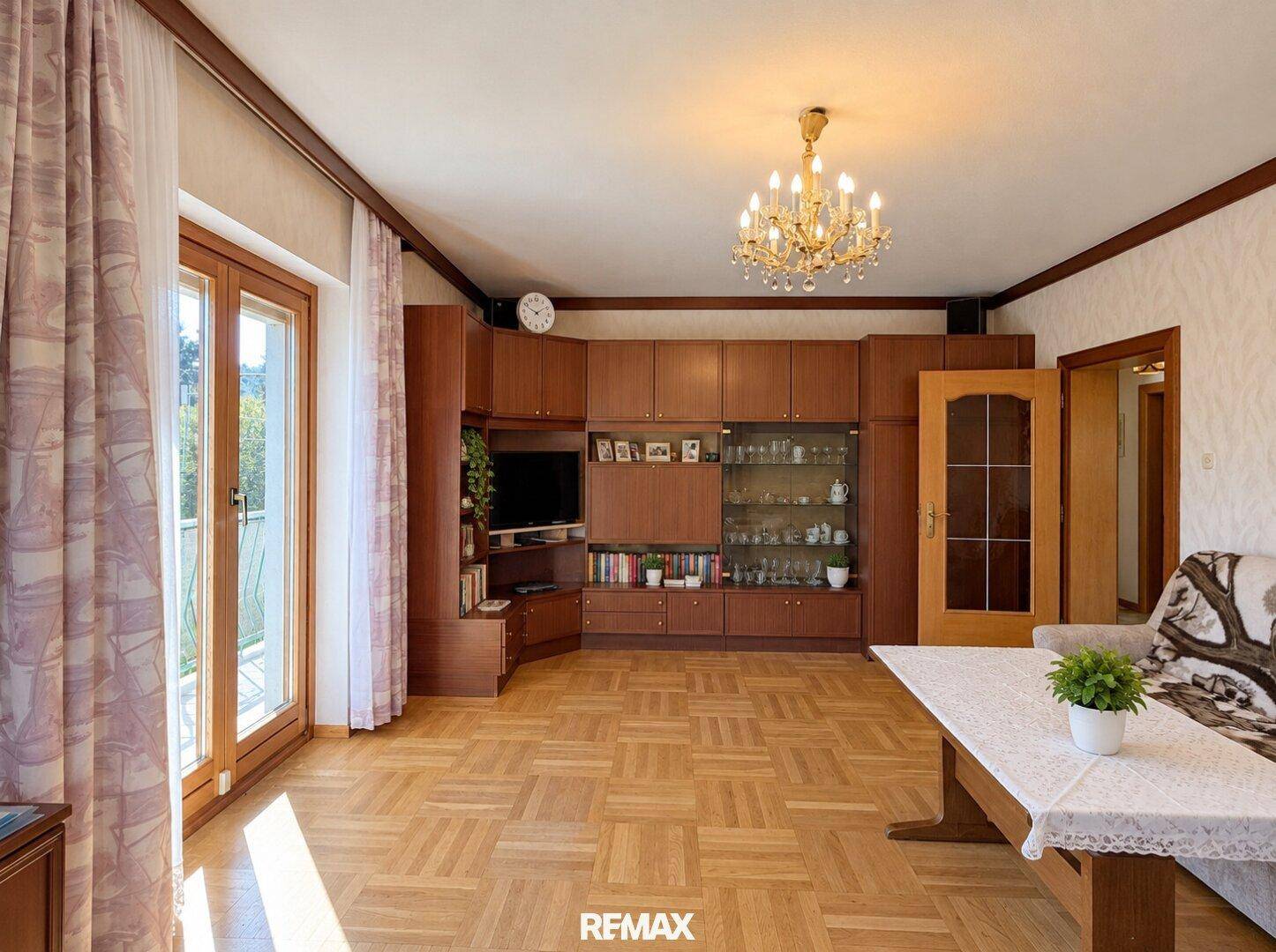 Geräumiges Wohnzimmer mit umfangreicher Holzschrankwand, Parkettboden und Balkonzugang.