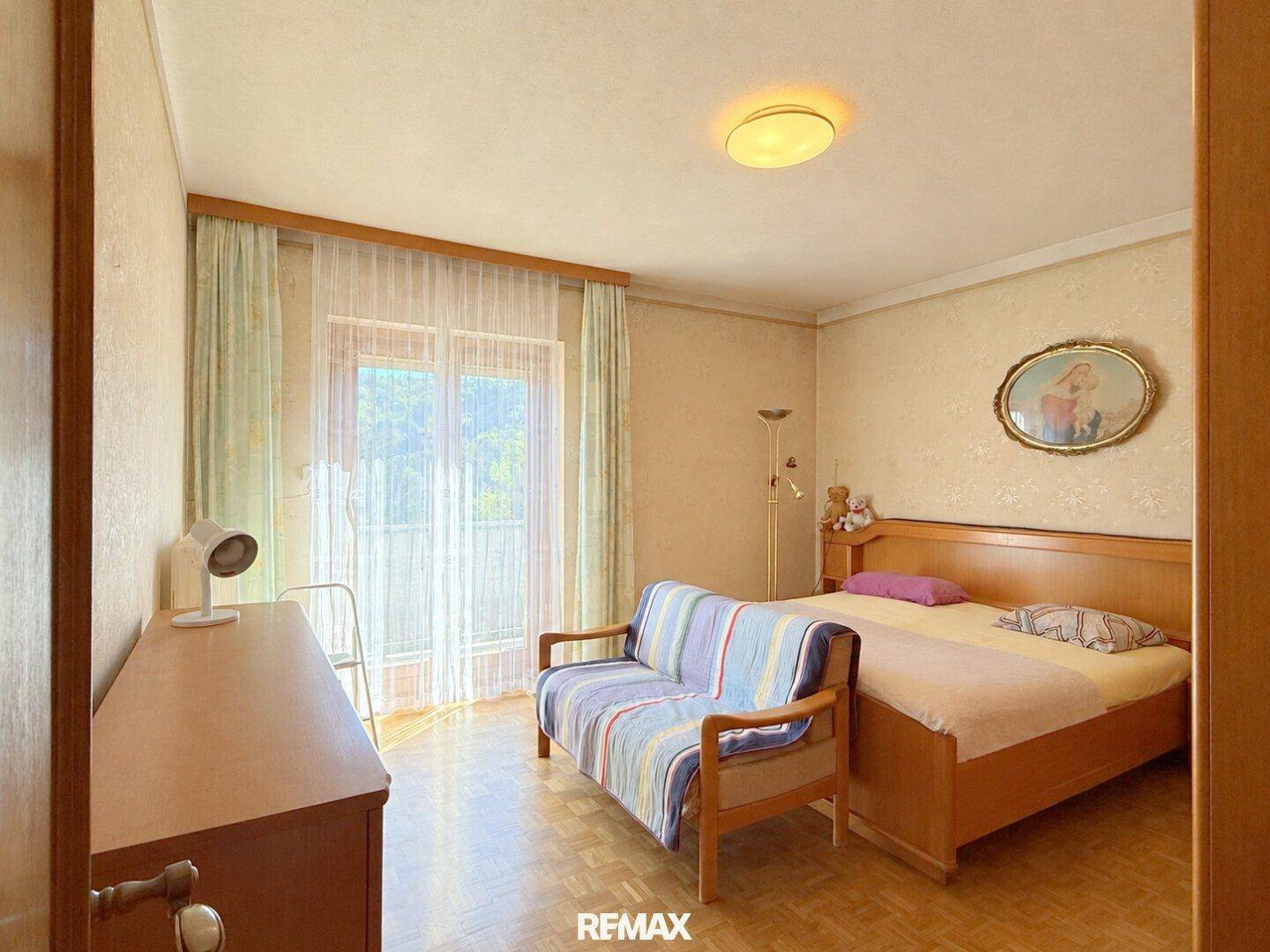 Gemütliches Schlafzimmer mit Holzbett, Sofa und Zugang zu einem französischen Balkon.