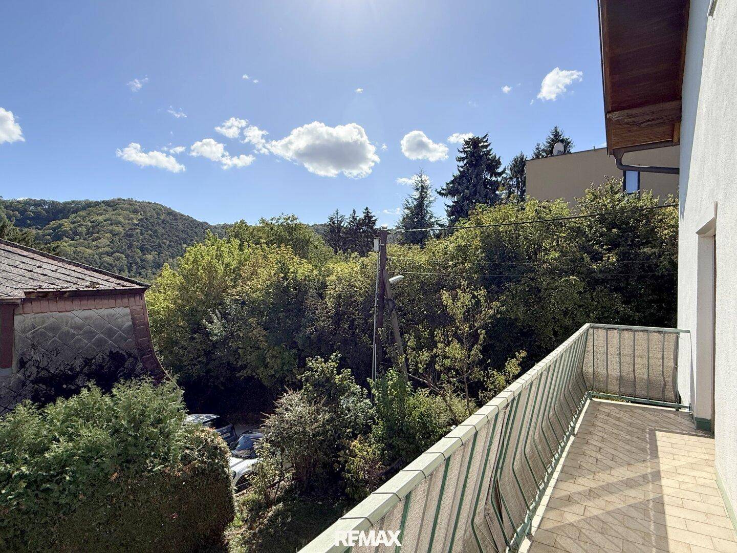Sonniger Balkon mit Metallgeländer und weitem Blick auf die grüne Umgebung und Berge.