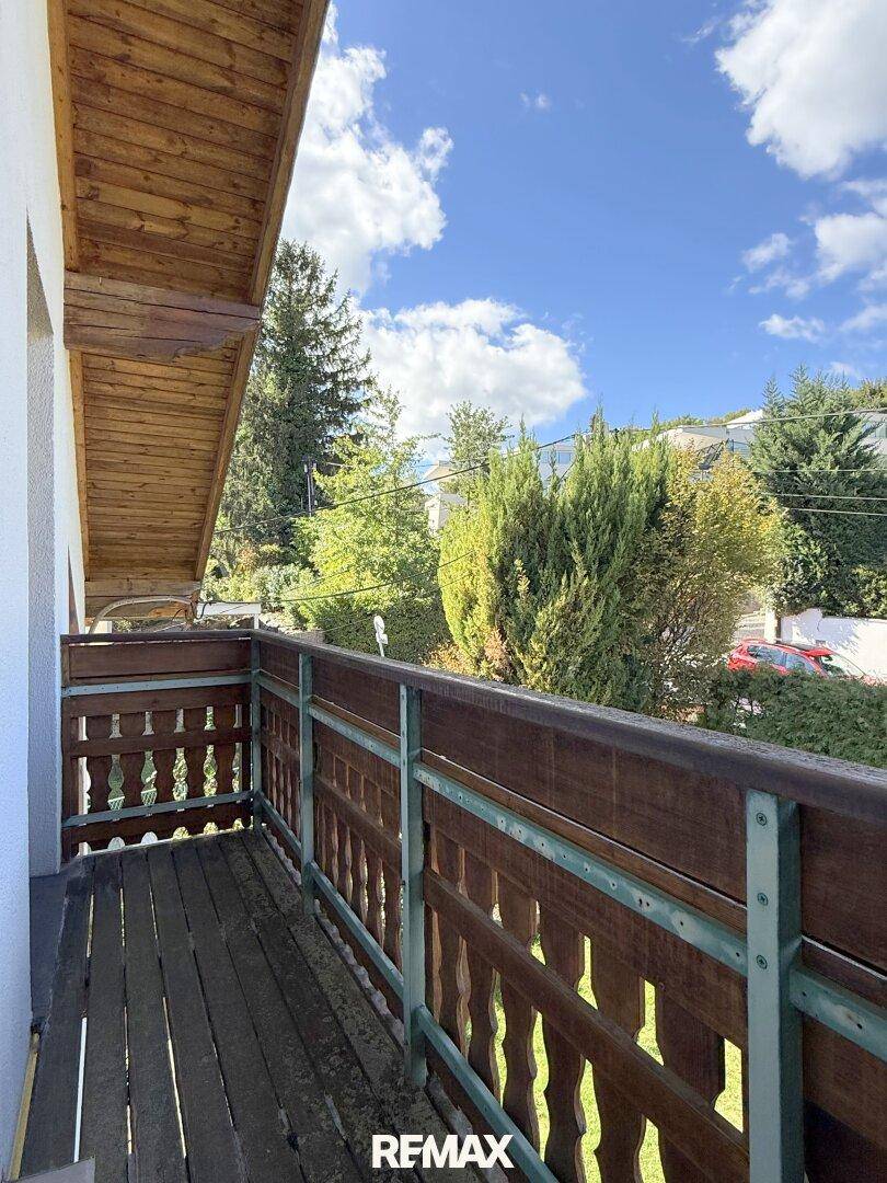 Überdachter Holzbalkon mit traditionellem Geländer und Blick auf die grüne Umgebung.