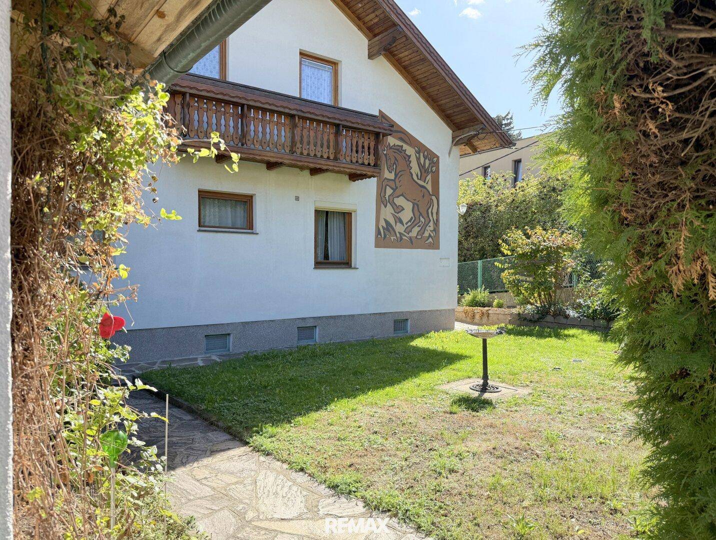 Seitenansicht des Hauses mit gepflegtem Rasen und üppiger Vegetation im Gartenbereich.