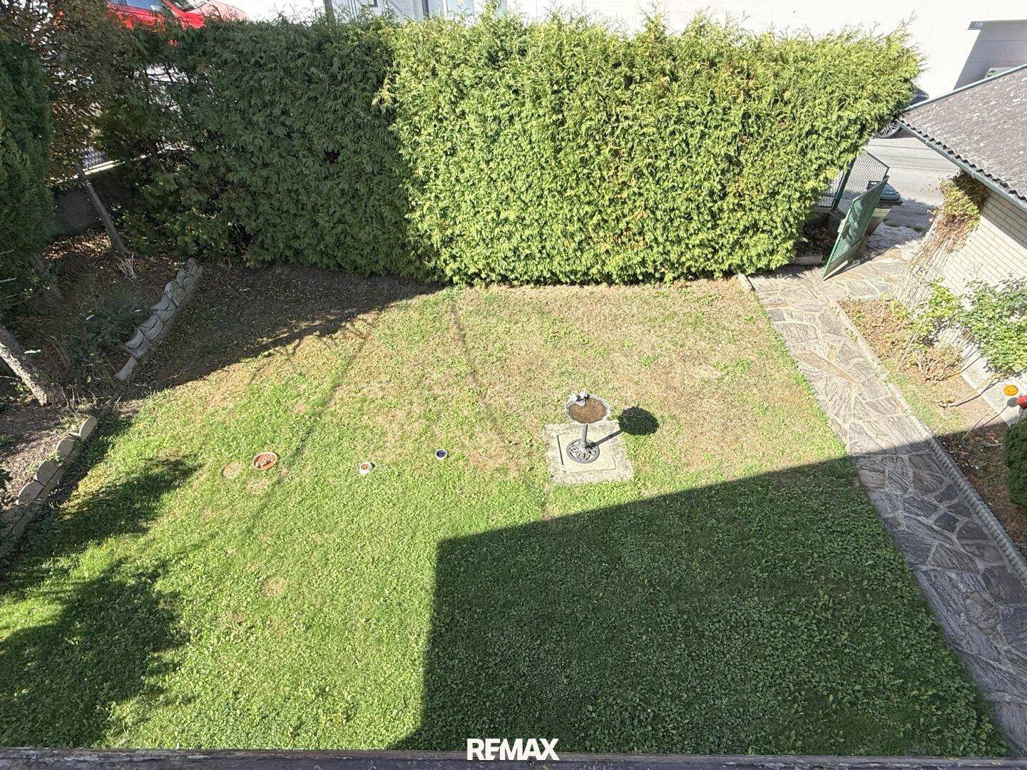 Vogelperspektive auf den Gartenbereich mit Rasenfläche, Steinweg und hoher Hecke.