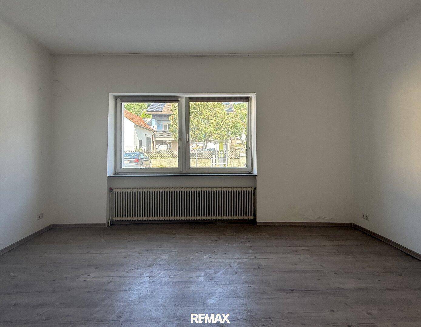 Leerer Wohnraum mit Laminatboden, weiß gestrichenen Wänden und großem Fenster.