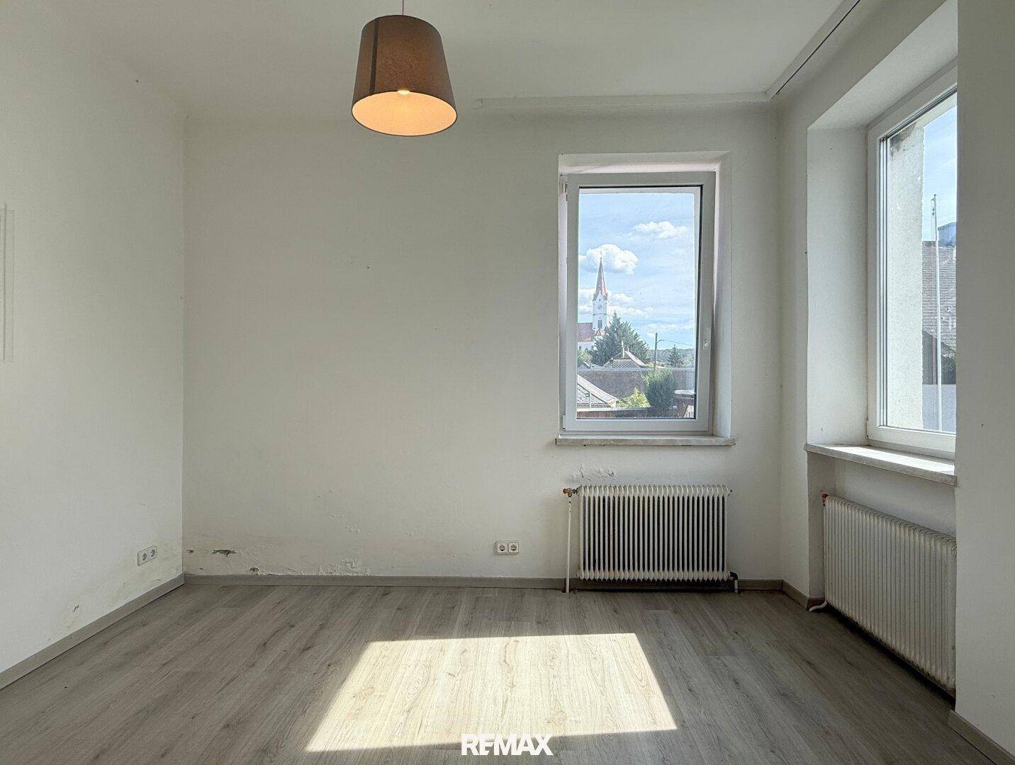 Helles Zimmer mit Laminatboden, Fenster und Blick auf die Umgebung.