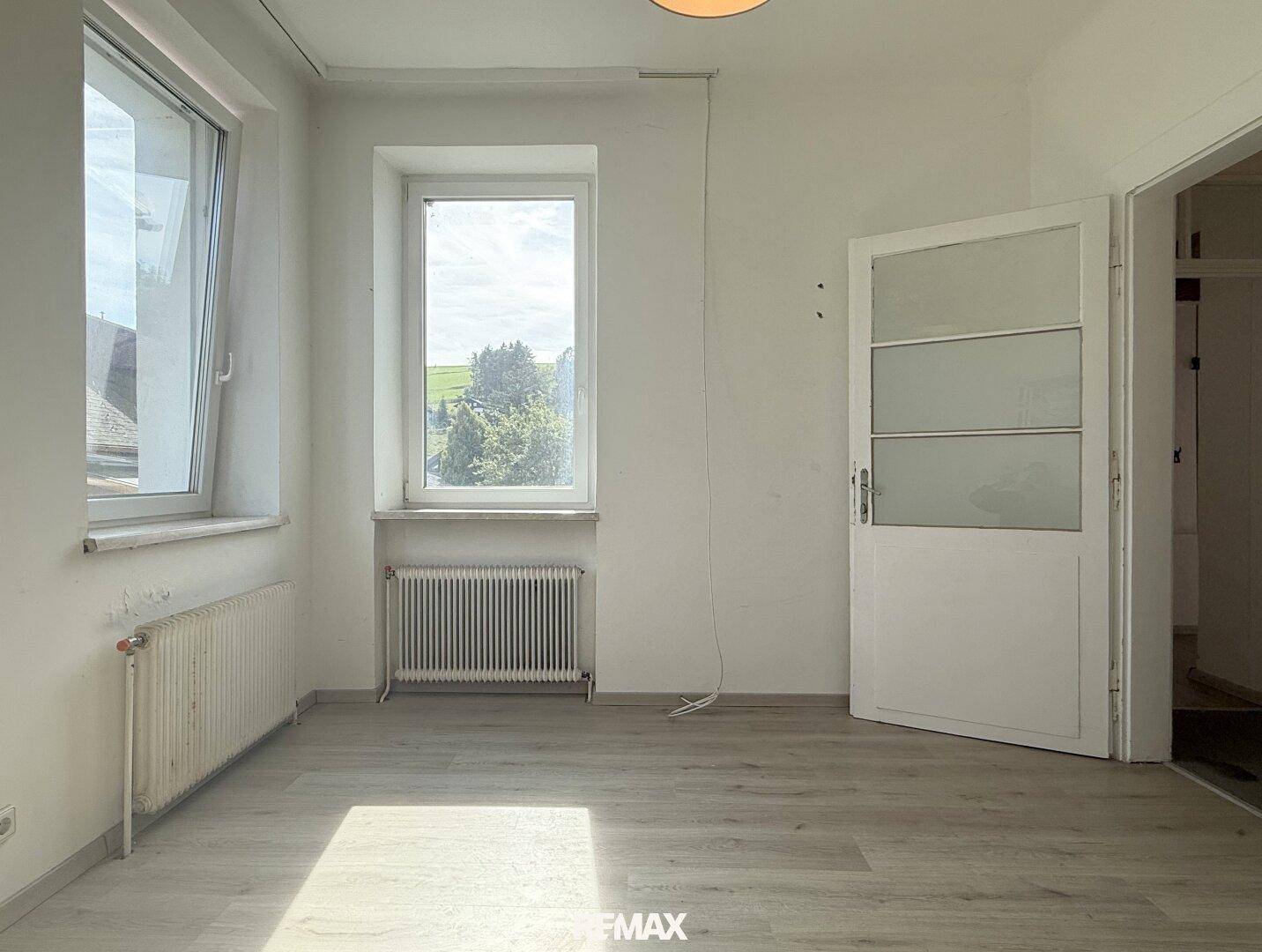 Geräumiges Zimmer mit Laminatboden, hellen Wänden und zwei Fenstern.