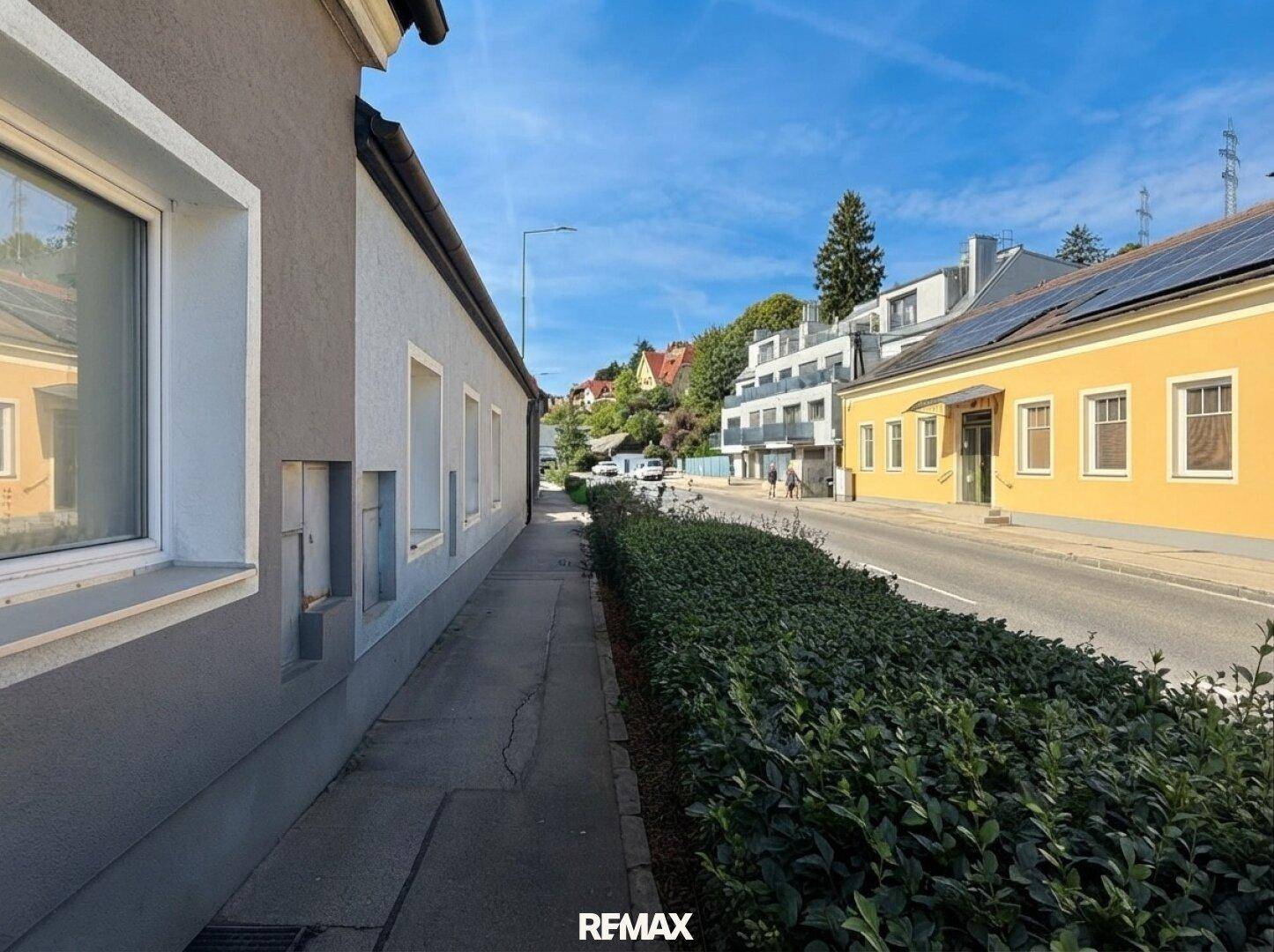 Seitenansicht des Hauses entlang einer Straße mit weiteren Gebäuden und Grünflächen.