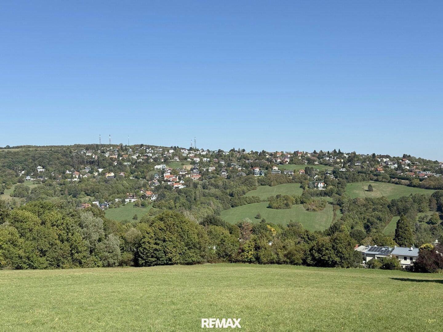 Malerischer Ausblick auf eine grüne Hügellandschaft mit einer dicht besiedelten Ortschaft.