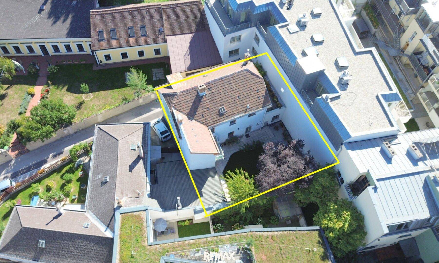 Luftaufnahme eines gepflegten Einfamilienhauses mit großem Garten, altem Baumbestand und Parkplatz in städtischer Umgebung.
