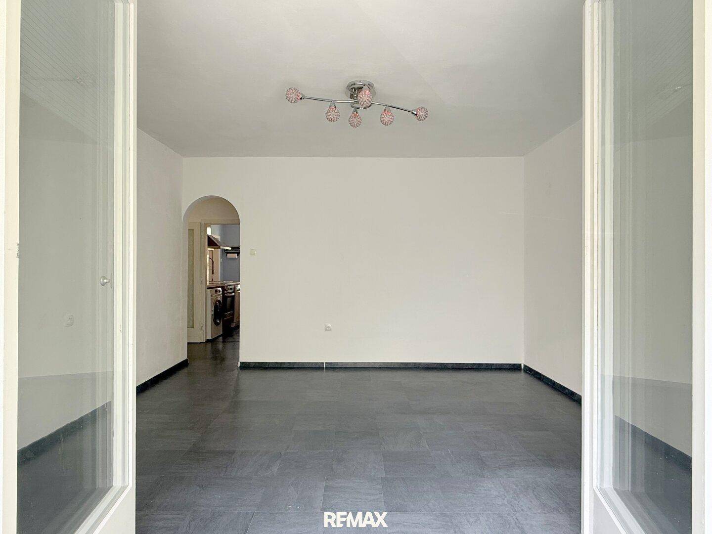 Geräumiges Wohnzimmer mit dunklem Fliesenboden und einem offenen Durchgang zu weiteren Räumen.